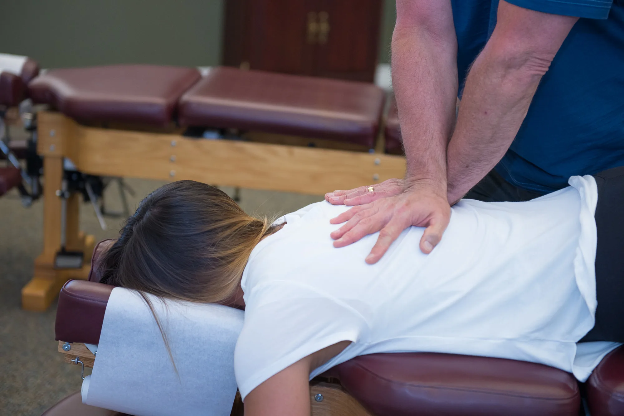 Chiropractor performing spinal adjustment on patient lying face down on treatment table.