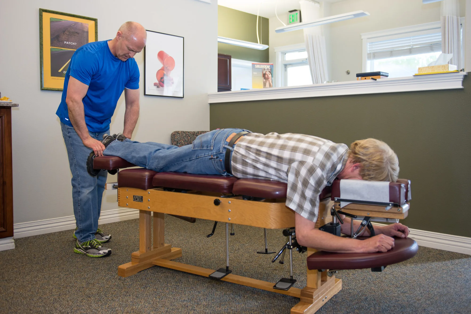 Chiropractor performing spinal adjustment on patient lying on treatment table.