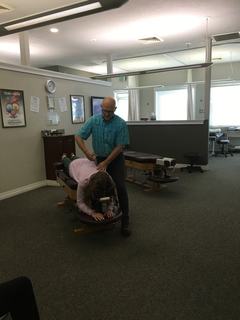 Chiropractor performing spinal adjustment on patient lying on treatment table in clinical room.