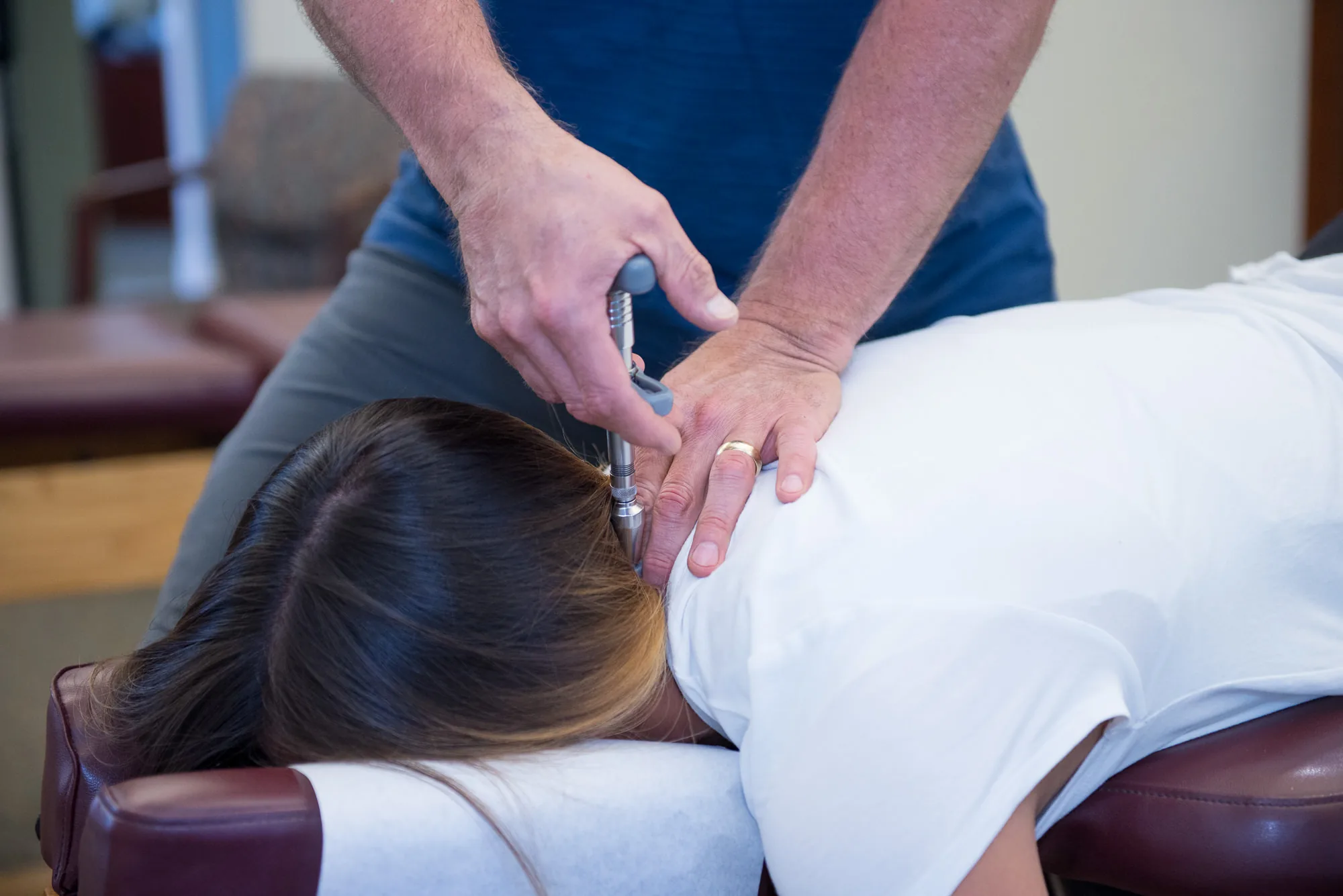 Chiropractor performing spinal adjustment on patient lying face down on treatment table.