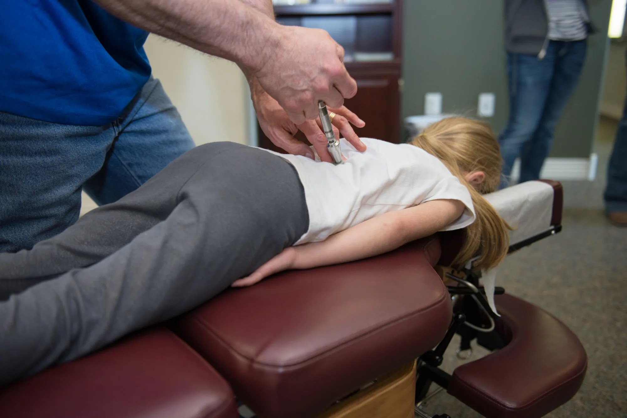Chiropractor performing spinal adjustment on young girl lying on treatment table.